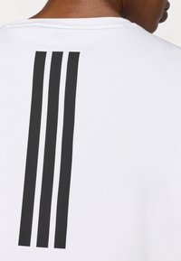 Λευκό T-shirt με τρεις κάθετες, παχιές μαύρες ρίγες στην πλάτη. Κατασκευασμένο από απαλό βαμβακερό ύφασμα με στρογγυλή λαιμόκοψη.