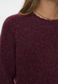 Burgundi színű kötött pulcsi puha, texturált felülettel és kerek nyakkivágással. Hullámos széllel és minimalista dizájnnal rendelkezik.