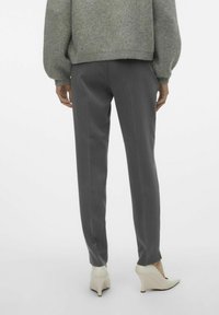 Pantaloni grigi su misura con una vestibilità slim, caratterizzati da una superficie liscia e sottili pieghe, abbinati a tacchi a cuneo color avorio.