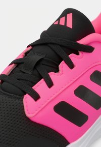 Zwarte sportschoen met roze synthetische overlays, gestructureerde zwarte stof, zwarte veters en drie zwarte strepen aan de zijkant.