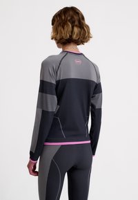 Długi rękaw sportowej bluzki w czerni i szarości z różowymi akcentami, o dopasowanym kroju, teksturowanej tkaninie i kontrastujących elementach wzorniczych.