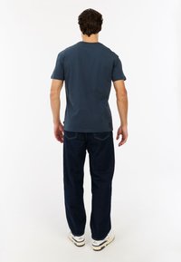 Donkerblauwe t-shirt met korte mouwen, gedragen met losse, donkere spijkerbroek en witte sneakers. T-shirt heeft een eenvoudig ontwerp zonder graphics.