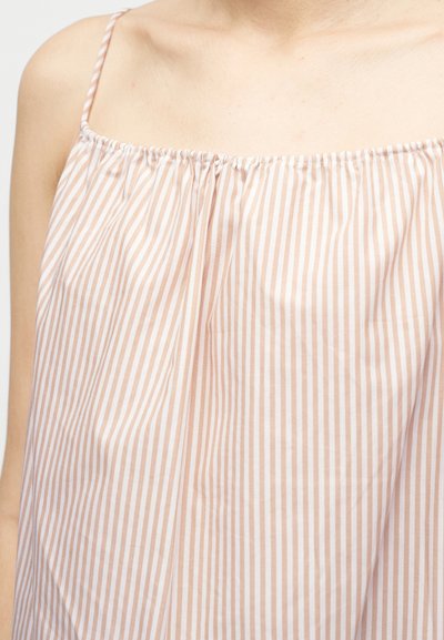 Približaj osebe, ki nosi ohlapno majico brez rokavov z tankimi naramnicami in navpičnimi bež in belimi črtami.