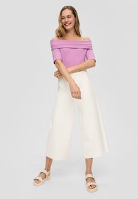 Horizonový top v levandulovej farbe s rebrovanou textúrou, skombinovaný s bielymi širokými nohavicami a béžovými pletenými sandálmi. Jednoduchý, elegantný dizajn.