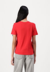 Camiseta corta roja de manga corta hecha de algodón, con un escote redondo y un ajuste relajado. Combinada con pantalones de mezclilla grises.