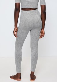Šedé bavlněné legíny s úzkým střihem a bezešvým designem, které mají elastický pás a hladkou texturu. Pozadí je jednobarevné.