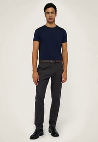 Tmavě modré přiléhavé tričko s krátkými rukávy, doplněné o tmavě šedé úzké kalhoty a hnědý kožený opasek. Kompletní outfit dotvářejí černé kotníkové boty.