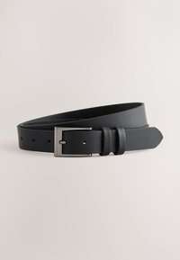 Ceinture en cuir noir avec boucle rectangulaire argentée, roulée sur un fond neutre.