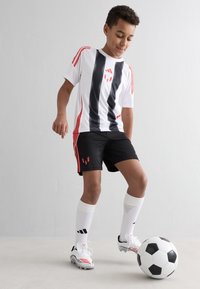 Ungdomsfotbollsdräkt med vit tröja med svarta ränder och röda detaljer, svarta shorts, vita strumpor och fotbollsskor. Boll vid fötterna.