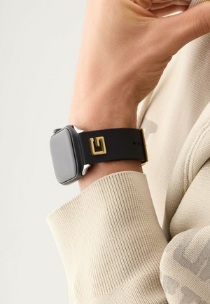 Black rubber strap watch with a square silver case, featuring a gold logo accent. The strap has a smooth texture and adjustable buckle.