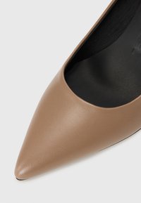 Escarpin beige en cuir à bout pointu avec une texture lisse et des bords bas, présent avec une semelle intérieure noire pour le contraste.