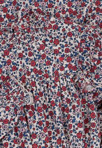 Bloemstof met kleine rode, roze en blauwe bloemen op een lichtbeige achtergrond; elastische ruches langs de randen.