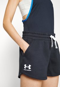 Černé bavlněné sportovní šortky s nastavitelným pasem, kapsami a bílým logem Under Armour na lemu. Hladká textura a dobře padnoucí střih.