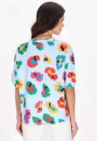 Kortærmet bluse i lysblåt stof med et farverigt blomsterprint i rød, grøn, gul og sort. Loose fit med detalje på bagsiden.