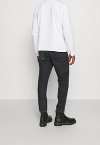 Svarta jeans med rak passform, kombinerat med en långärmad vit skjorta. Outfiten har svarta kängor som går till anklarna och en enkel design.