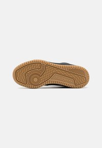 Svart sneaker med en texturerad gummiyttersula som har en gummsula och framträdande Adidas-logotyp. Mönstret inkluderar spår och kurvor.