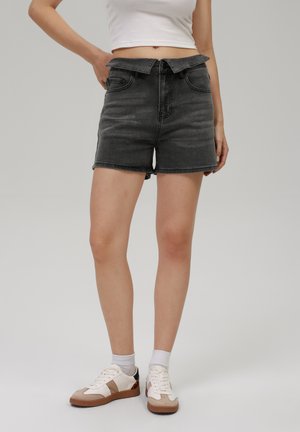 Black denim shorts with a high waist, featuring a fitted design, belt loops, and front pockets. Paired with white sneakers and ankle socks.