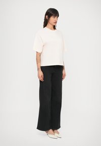 Camiseta de manga corta de color rosa claro con un ajuste relajado, combinada con jeans negros de pierna ancha y talle alto, y zapatos planos blancos con punta estrecha.