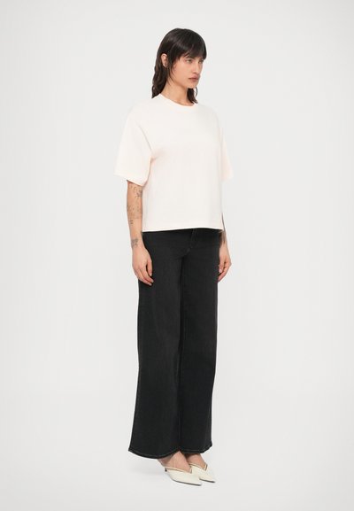 Light pink short-sleeve t-shirt with a relaxed fit, paired with high-waisted black wide-leg jeans and white pointed flats.