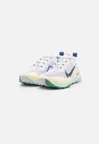 Zapatillas de correr Nike con una parte superior de malla blanca, acentos multicolores, suela gris y verde, y un diseño curvado. Cuentan con cierre de cordones y lengüetas para facilitar su colocación.