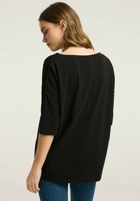 Czarny, oversize top z szerokim dekoltem, rękawami o długości trzech czwartych i gładką teksturą materiału. Design zapewnia luźny fason, idealny do codziennego noszenia.