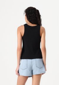 Black ribbed tank top with a rounded neckline, fitted shape, and sleeveless design. Worn with light blue denim shorts.