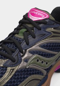 Κοντινό πλάνο ενός ναυτικού και ελιάς αθλητικού παπουτσιού Saucony με μαύρα κορδόνια, λεπτομέρειες από δίχτυ και ροζ λογότυπο στη γλώσσα.