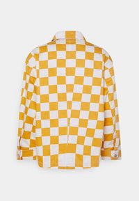 Żółto-biała koszula w kratę z długimi rękawami, mankietami na guziki, klasycznym kołnierzem i prostym dołem; tekstura bawełnianej tkaniny.