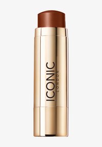 Fond de teint en stick dans un tube cylindrique doré, avec un sommet marron foncé et la marque "ICONIC LONDON" en noir sur le côté.