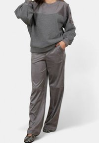 Felpa grigia con un pannello superiore testurizzato, abbinata a pantaloni larghi grigi lucidi. Scarpe slip-on nere con pois bianchi.