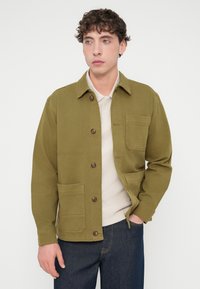 Χακί πράσινο μπουφάν με γιακά, κουμπώματα και δύο τσέπες μπροστά. Κατασκευασμένο από ανθεκτικό ύφασμα με ομαλή υφή.