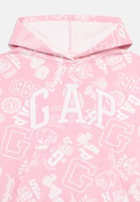 Moletom rosa com letras brancas "GAP" em grande formato e vários logos e designs menores da GAP impressos por todo o lado.