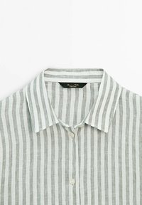 Chemise en lin léger avec des rayures verticales grises et blanches, un col classique et une fermeture à boutons à l'avant. Étiquette visible à l'intérieur du col.