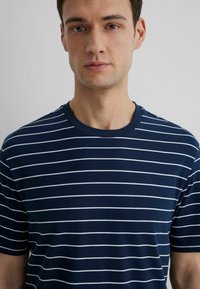 Navy blue striped t-shirt with short sleeves, featuring thin white horizontal stripes and a round neckline. Soft cotton texture.