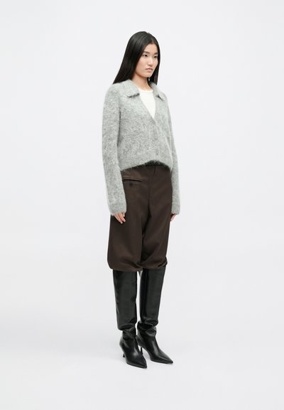 Jasnoszary, puszysty kardigan z kołnierzem, zestawiony z brązowymi, luźnymi spodniami i zaoczami na wysokim obcasie w kolorze czarnym. Prosty, nowoczesny design.
