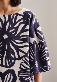 Top blu navy con motivo floreale bianco, con scollo ampio, maniche corte e vestibilità rilassata. Realizzato in un tessuto morbido e leggero.