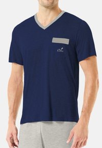 Camiseta de cuello en V azul marino de tejido suave, con un cuello gris a modo de acento, bolsillo en el pecho izquierdo y un sutil detalle de logo. Corte casual y mangas cortas.