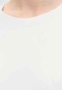 Gros plan d'une personne portant un t-shirt blanc uni à col rond montrant le cou et le haut de la poitrine.