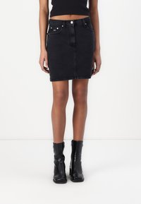 Svart denim mini kjol med fem fickor, metallknappstängning och subtila sömnadsdetaljer. Matchas med svarta anklar stövlar.