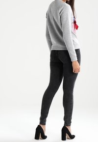 Felpa grigia con un design colorato davanti, abbinata a jeans neri aderenti e scarpe con tacco nere.