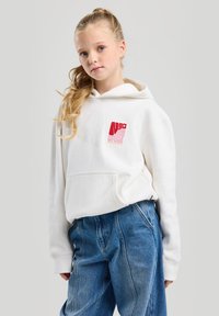 White cotton hoodie with front pocket, featuring a red NYC logo. Paired with high-waisted blue denim jeans. Smooth texture and relaxed fit.