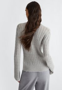 Maglione grigio lavorato a maglia con un design a coste testurizzato. Maniche lunghe con una vestibilità morbida. Materiale leggero e soffice, abbinato a pantaloni grigi.