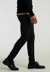 Mörkblå, slim-fit rutiga byxor med subtil textur. Bärs med en långärmad svart tröja och svarta kostymskor.