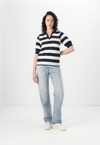 Gestreepte polo met korte mouwen in marineblauw en roomkleur, met een V-hals ontwerp. Gecombineerd met lichtblauwe wijde jeans en witte sneakers.