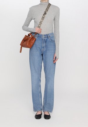 Persona che indossa una maglietta a maniche lunghe grigia chiara e jeans blu, mentre tiene una borsa in pelle marrone con tracolla nera Emporio Armani e scarpe ballerine nere.