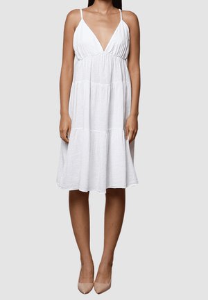 Vestido de lino blanco con un profundo escote en V y tirantes finos. Presenta un diseño en capas y cae por debajo de la rodilla. Tela ligera y texturizada.