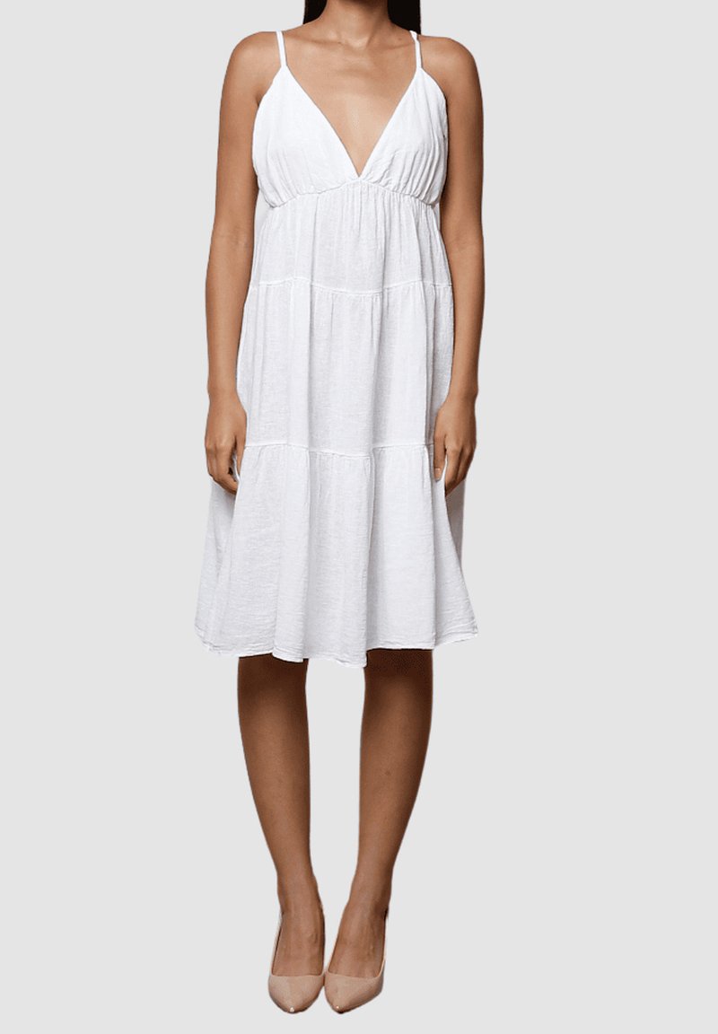Vestido de lino blanco con un profundo escote en V y tirantes finos. Presenta un diseño en capas y cae por debajo de la rodilla. Tela ligera y texturizada.