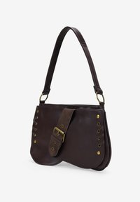 Bolso de hombro de cuero marrón oscuro con correa ancha, detalle de hebilla central y acentos de remaches de latón en los lados sobre fondo blanco.