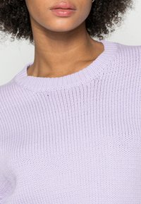 Licht lavendel gebreide trui met een ribbelstructuur en een ronde halslijn. Close-up weergave, die de zachte afwerking van de stof en de gelijkmatige steken toont.