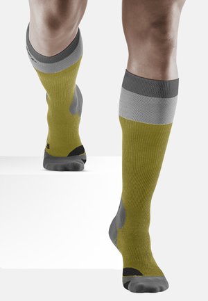 Kompressionssocken in olivgrün mit grauen und schwarzen Akzenten. Mit gerippter Textur, knielangem Design und verstärktem Zehenbereich.